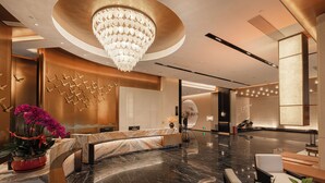 Eine moderne Lobby mit einem Marmor-Empfangstresen, einer Kandelaber-Leuchte und einer Wand mit Vogel-Skulpturen.
