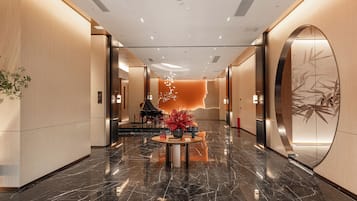 A modern hotel lobby with a marble floor, a grand piano, and a decorative wall with a bamboo motif.