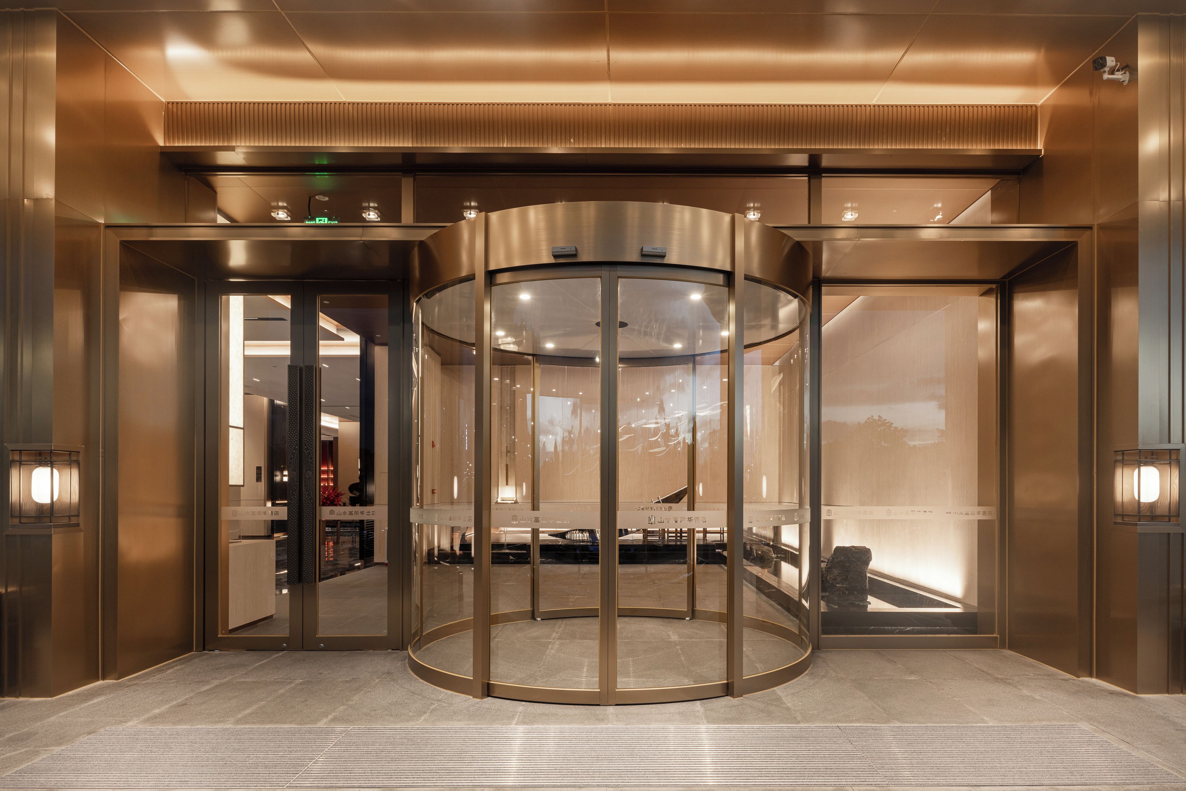 A revolving door with glass panels and a metallic frame, leading to a lobby area with a reception desk and seating.
