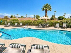 A swimming pool with lounge chairs and a table, surrounded by a fence and palm trees.