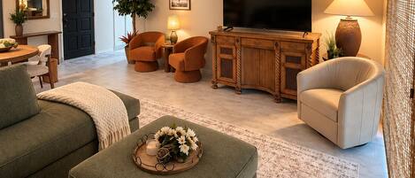 A living room with a sofa, ottoman, TV, and a plant.