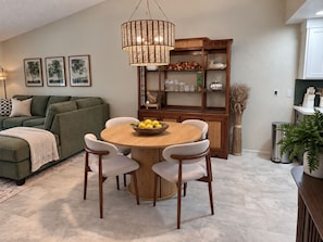 Een moderne woonkamer met een ronde houten eettafel, witte stoelen, een groene bank en een houten kast met glazen deuren.