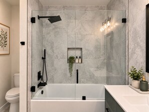 Ein modernes Badezimmer mit einer gläsernen Duschkabine, einer weißen Badewanne und einer kleinen Ablage für Pflegeprodukte.