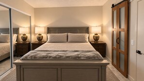 Ein Schlafzimmer mit einem großen Bett, zwei Nachttischen mit Lampen, einem Schrank mit Schiebetür und einem Spiegel an der Wand.