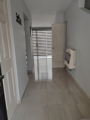 Un passadís amb una porta, un aire condicionat fixat a la paret i una finestra amb persianes.