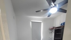 Ein kleines Schlafzimmer mit zwei Einzelbetten, einem Deckenventilator, einem Fenster und einem Kleiderschrank.