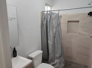 Un bany amb vàter, rentapel i cortina de dutxa, i parets de rajola.