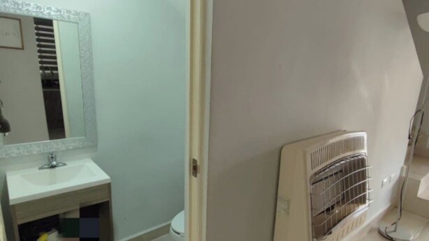 Ein Badezimmer mit Waschbecken, Spiegel und Toilette. An der Wand befindet sich ein Heizkörper und ein Ablagefach mit Pflegeprodukten.