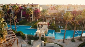 Ein Resort mit einem zentralen Swimmingpool, Palmen und einer überdachten Sitzgelegenheit im Freien.