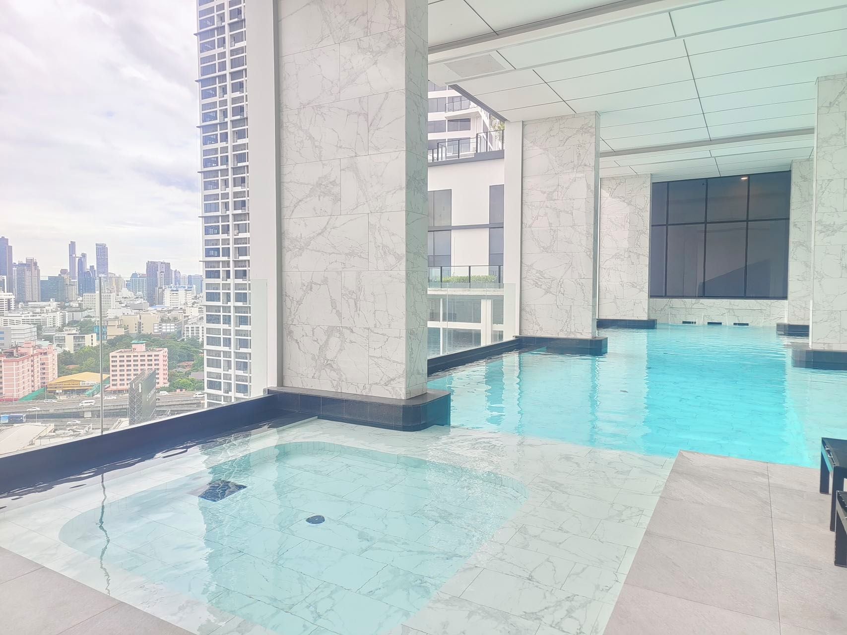 Una piscina en la azotea con vistas a la ciudad, baldosas de mármol y una barandilla de cristal.
