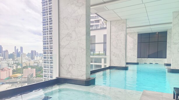 Una piscina en la azotea con vistas a la ciudad, baldosas de mármol y una barandilla de cristal.