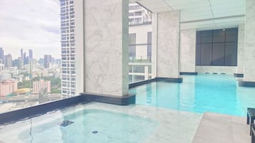 Una piscina en la azotea con vistas a la ciudad, baldosas de mármol y una barandilla de cristal.