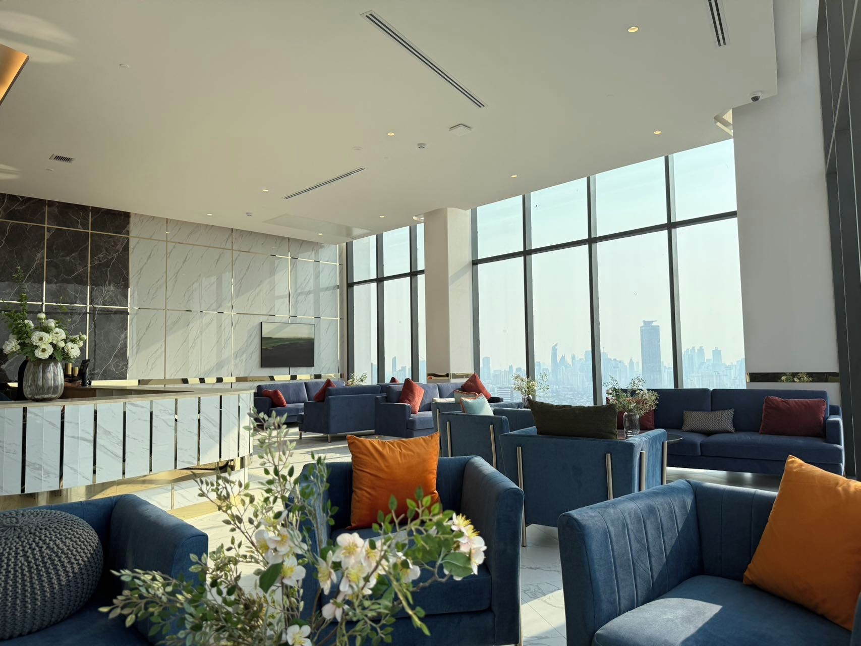 A spacious lounge area with multiple seating options, a marble accent wall, and a cityscape view through large windows.
