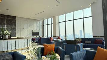 A spacious lounge area with multiple seating options, a marble accent wall, and a cityscape view through large windows.