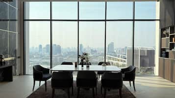 A modern dining area with a large table and chairs, large windows offering a city view, and a minimalist decor.