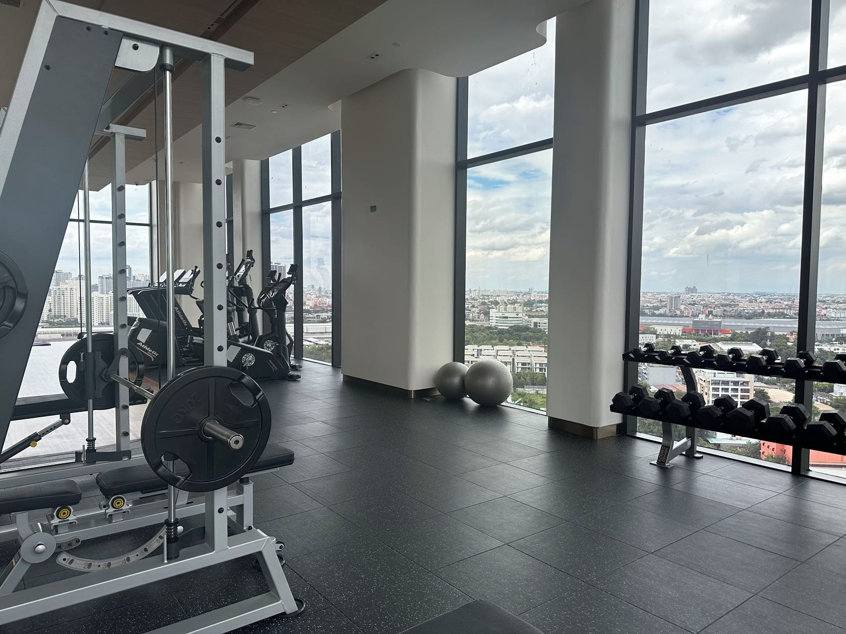 Une salle de sport équipée de matériel d’exercice, dotée de grandes fenêtres et offrant une vue sur la ville.