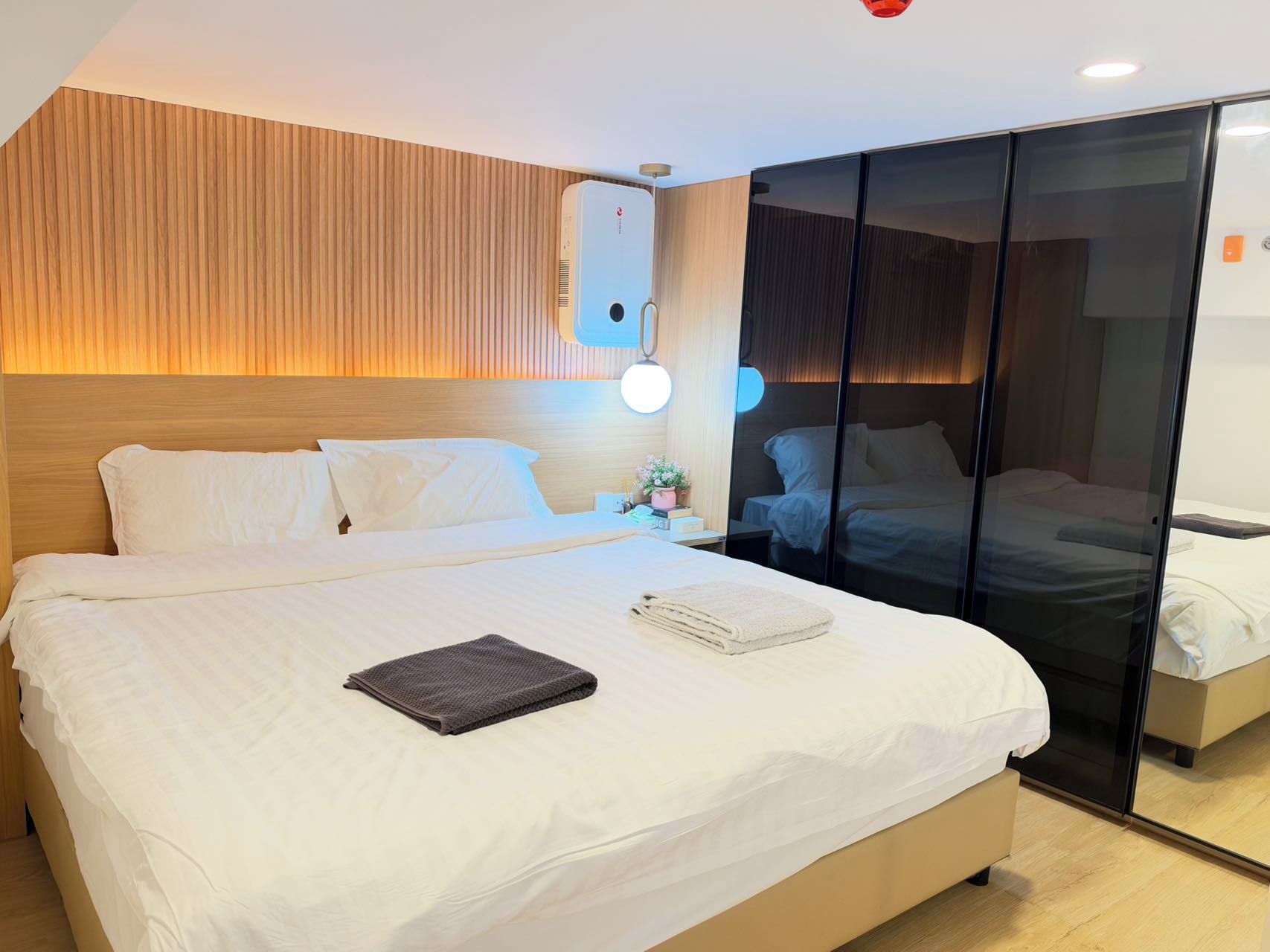 A hotel room with a large bed, a bedside table with a lamp, and a sliding door leading to another room.