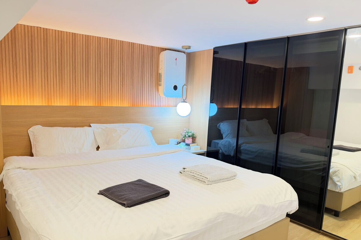 Habitació d'hotel amb un llit gran, una tauleta de nit amb una làmpada i una porta corredissa que dona a una altra habitació.