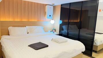 A hotel room with a large bed, a bedside table with a lamp, and a sliding door leading to another room.