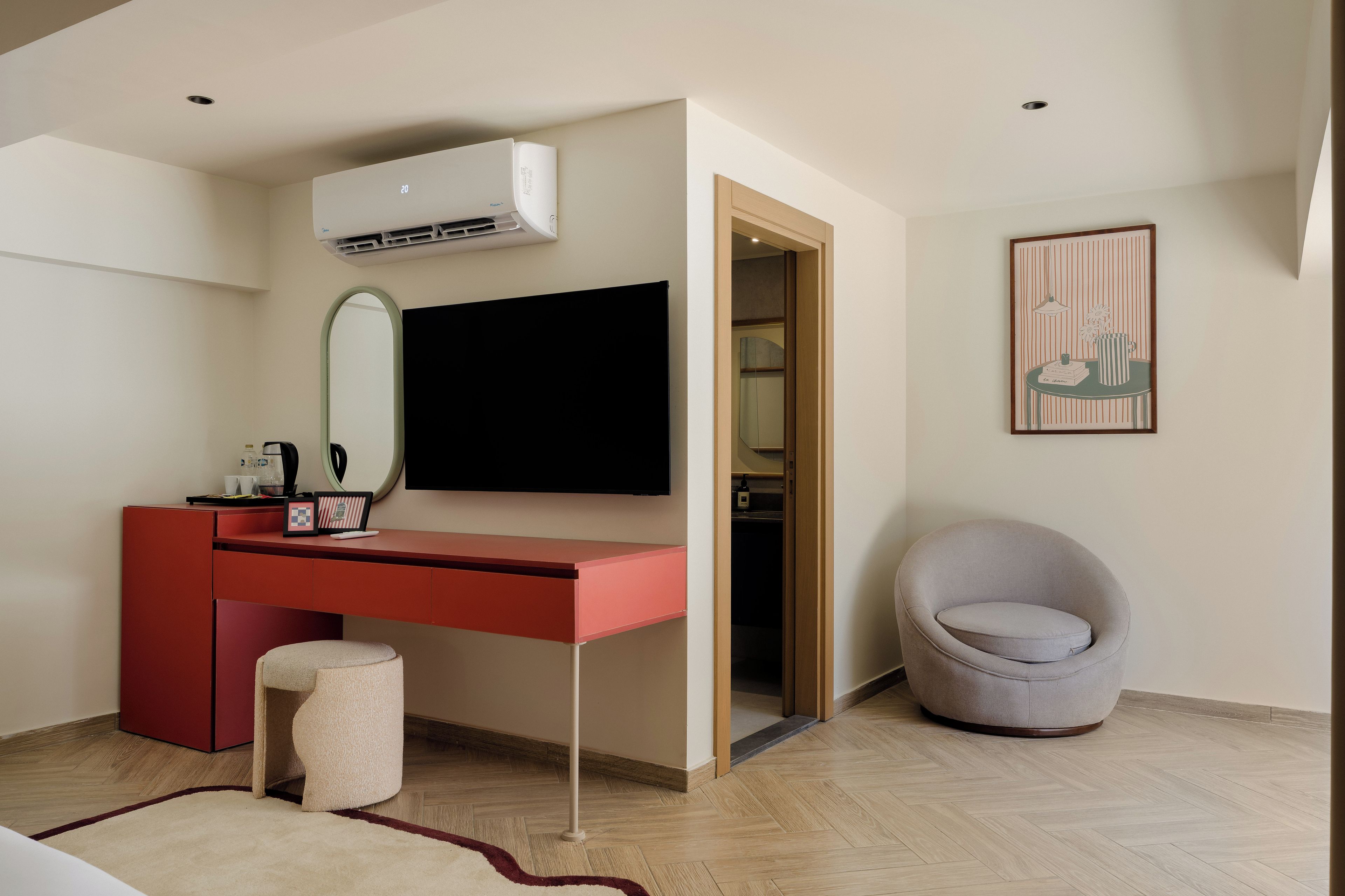 A modern bedroom with a red desk, a grey bean bag chair, a large mirror, and a flat-screen TV.
