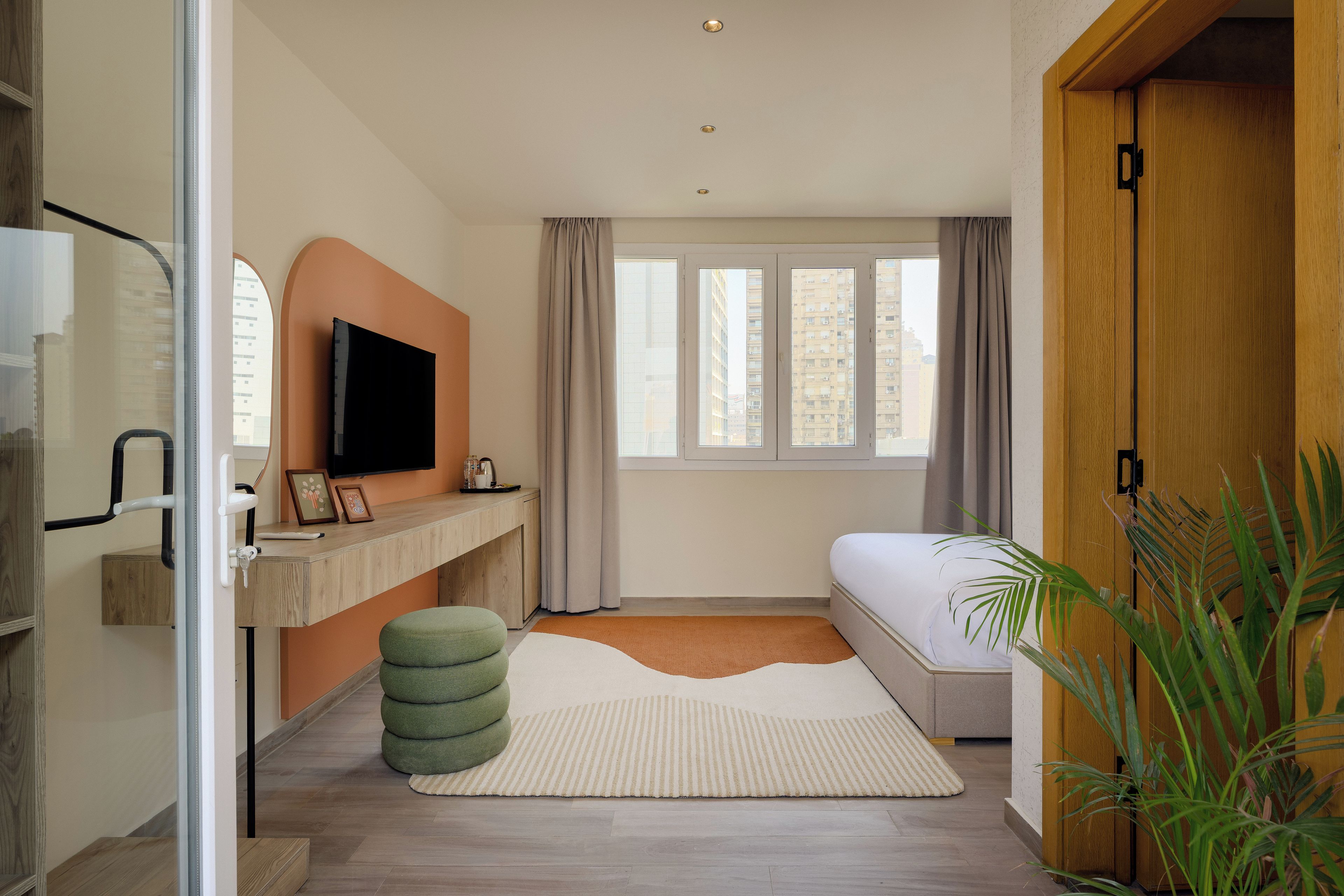 Un dormitorio moderno con cama, escritorio, televisor y ventana con cortinas.