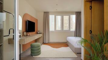 Un dormitorio moderno con cama, escritorio, televisor y ventana con cortinas.