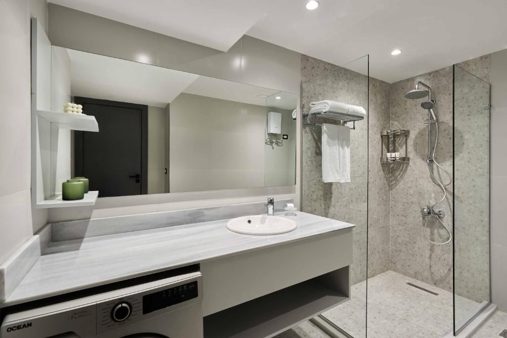 Un baño moderno con un espejo grande, un lavamanos y una zona de ducha con paredes de vidrio.