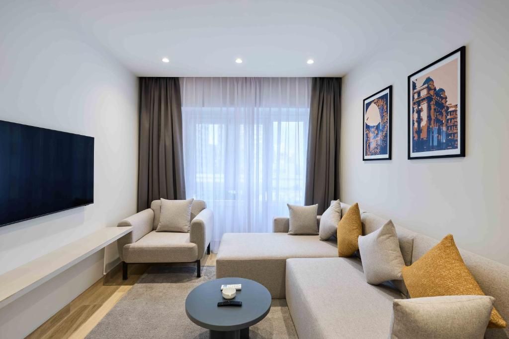 A modern living room with a flat-screen TV, two sofas, a coffee table, and a large window with curtains.