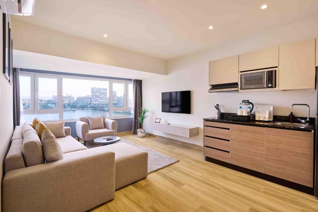 A modern living room with a sofa, a coffee table, and a TV. There's a kitchen area with a microwave and cabinets.