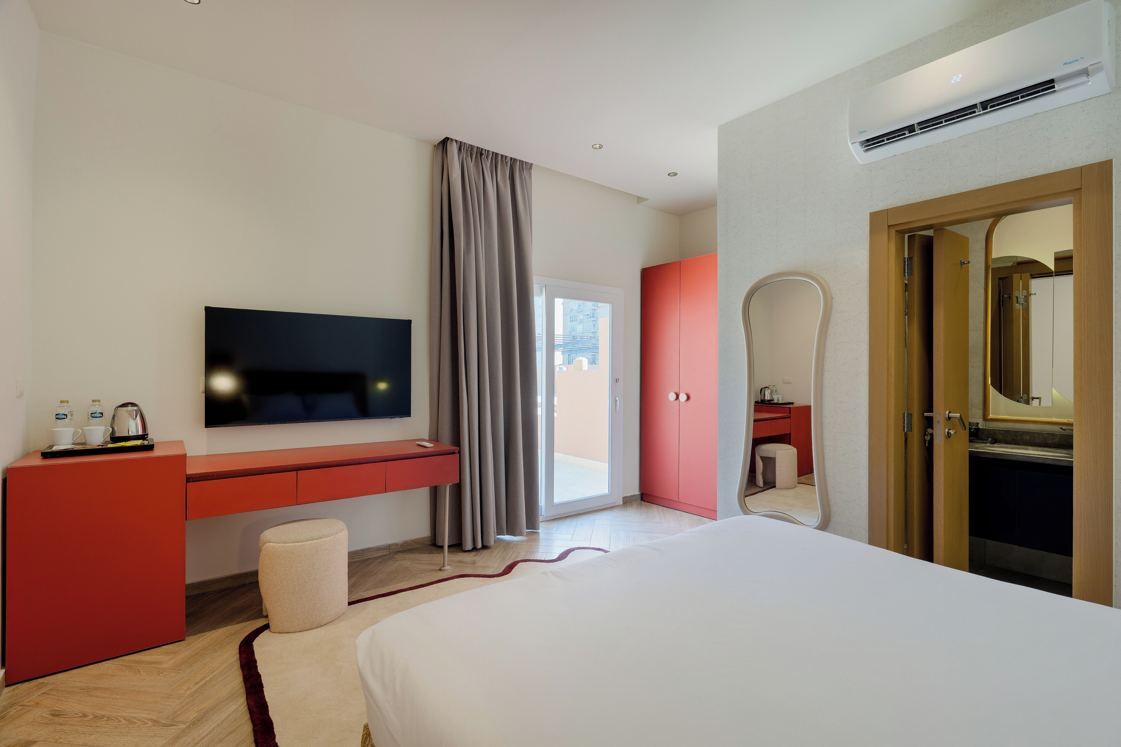 Habitación de hotel con cama, televisión, escritorio con silla, armario, baño con espejo y una puerta.