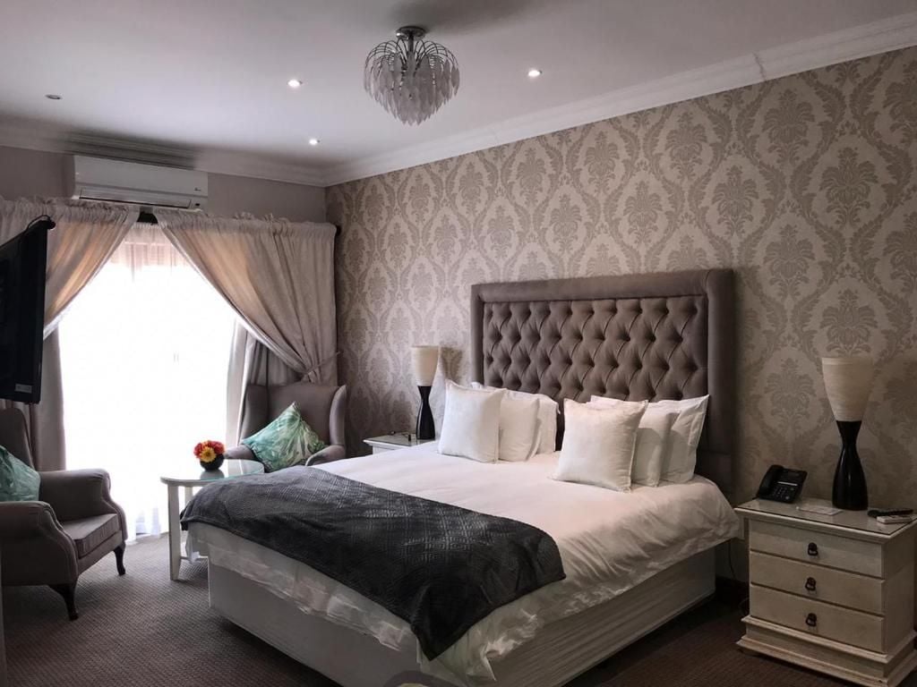 Una camera d'albergo con un letto grande, un comodino, una sedia e una lampada decorativa.