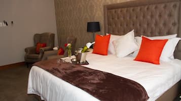 Una camera d'albergo con un letto grande, una poltrona, una lampada e un vaso con fiori.