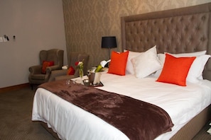 A hotel room with a large bed, a chair, a lamp, and a vase with flowers. - Classique  Grace Boutique Hotel and Spa (Morningside Manor)