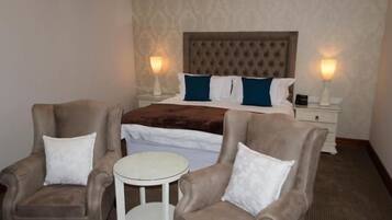 Una habitación de hotel con una cama, dos sillones, una mesita redonda y dos lámparas de noche.