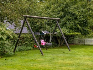 Un columpio de madera en un jardín exuberante con una casa al fondo.
