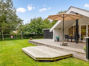 Una terraza de madera con un columpio y un porche cubierto con mobiliario exterior.