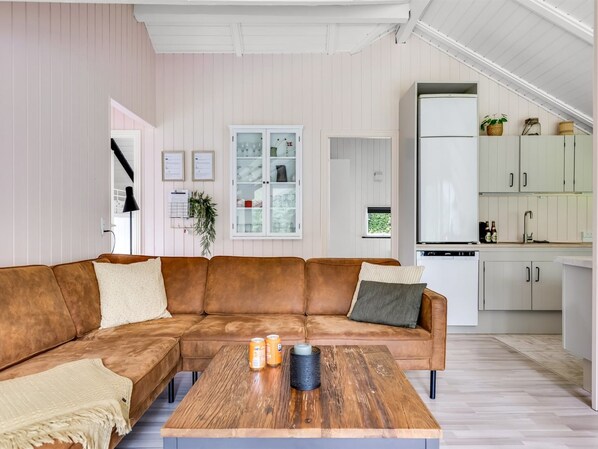 Una sala moderna con un sofá seccional marrón, una mesa de centro de madera y una cocina con armarios blancos.