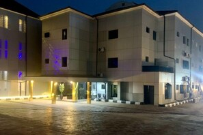 Un edificio de varios pisos con fachada plana, ventanas amplias y una zona de acceso cubierta con un camino que lleva a la entrada principal.