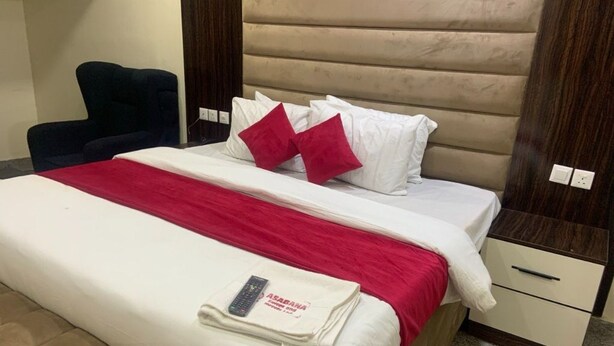 A hotel room with a bed, a chair, a nightstand, and a bedside table. - Asabana Suites and Hotels Enugu (Enugu)
