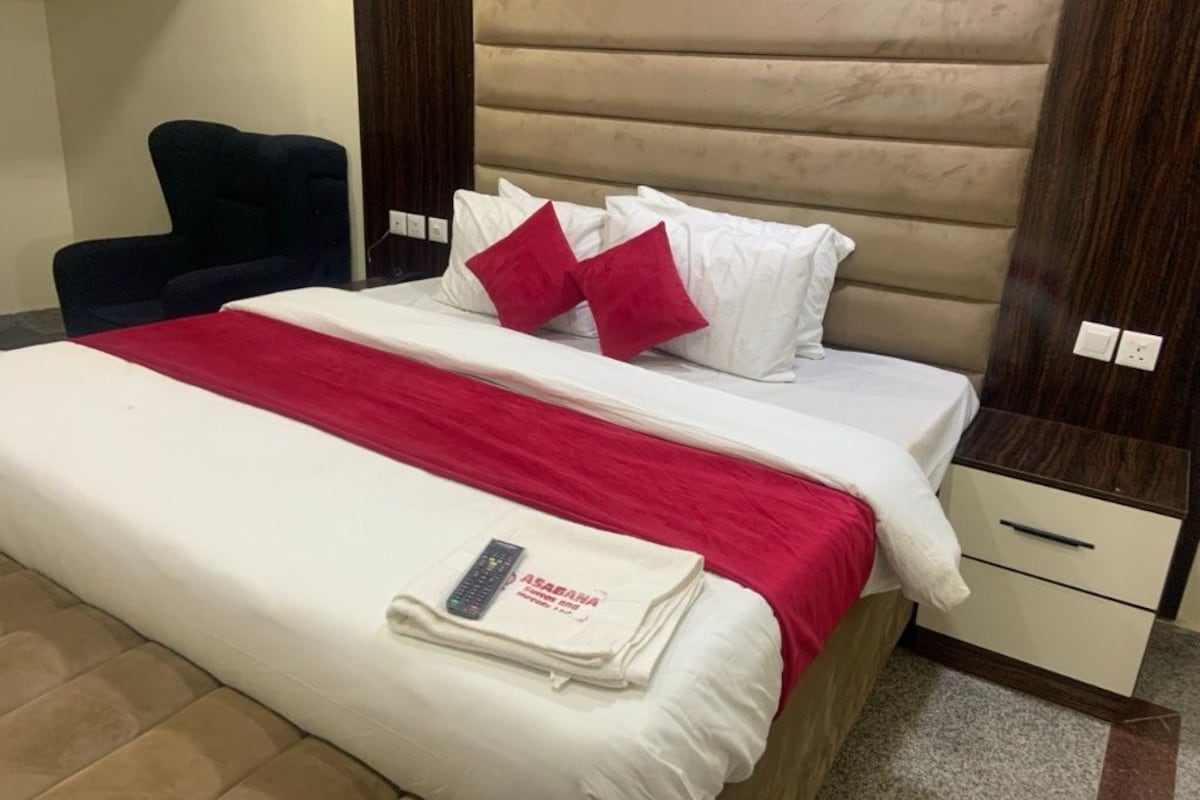 Una habitación de hotel con cama, una silla, una mesita de noche y una mesita auxiliar.