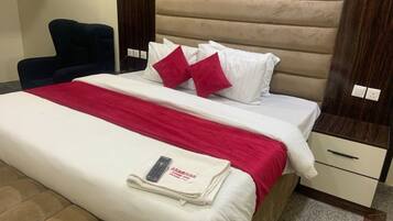 Una habitación de hotel con cama, una silla, una mesita de noche y una mesita auxiliar.