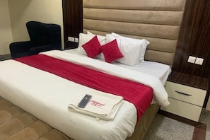 A hotel room with a bed, a chair, a nightstand, and a bedside table. - Asabana Suites and Hotels Enugu (Enugu)