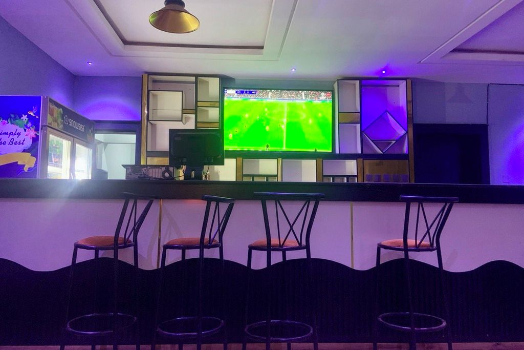 A bar area with a television displaying a sports event, bar stools, and a decorative wall.
