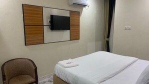A hotel room with a bed, a chair, a flat-screen TV mounted on a wooden panel, and an air conditioning unit. - Asabana Suites and Hotels Enugu (Enugu)
