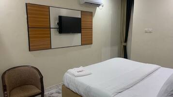 Habitación de hotel con cama, una silla, un televisor de pantalla plana montado en un panel de madera y un equipo de aire acondicionado.
