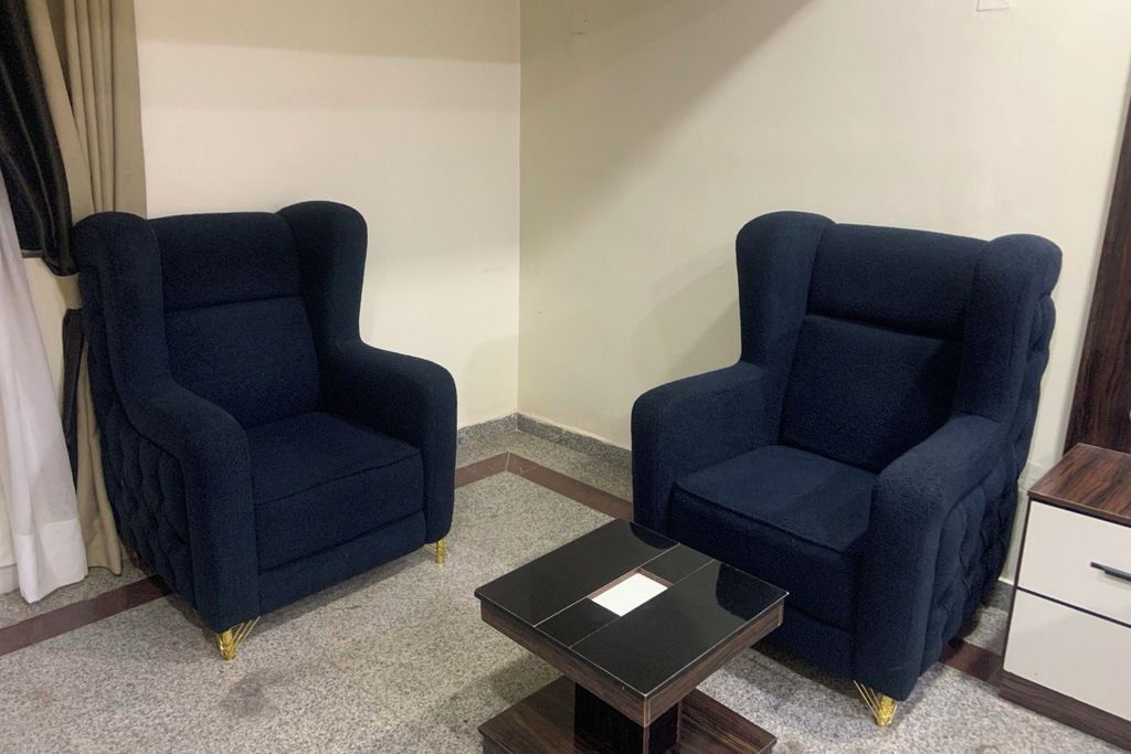 Una habitación con dos sillones azul oscuro, una mesita negra y un mueble blanco.