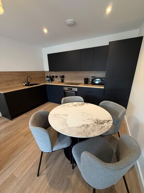 Una cocina moderna con armarios oscuros, una mesa redonda de mármol y sillas tapizadas en gris.