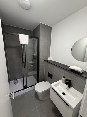 A modern bathroom with a glass-enclosed shower, a toilet, and a sink with a mirror above. - Standard Two Bedroom Apartment Near MediaCity (Salford)