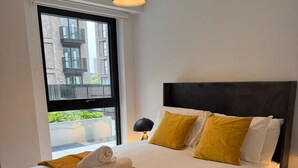 Ein modernes Hotelzimmer mit einem großen Bett, einem Fenster mit Blick auf Gebäude, einer Nachttischlampe und einem ordentlich bezogenen Bett mit einem Handtuch.
