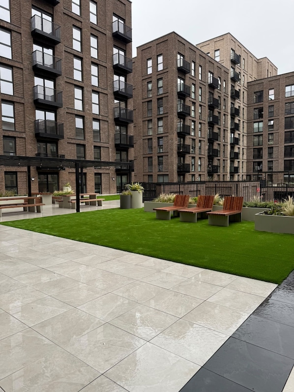 A modern apartment building with multiple balconies, a courtyard with seating, and a well-maintained lawn.